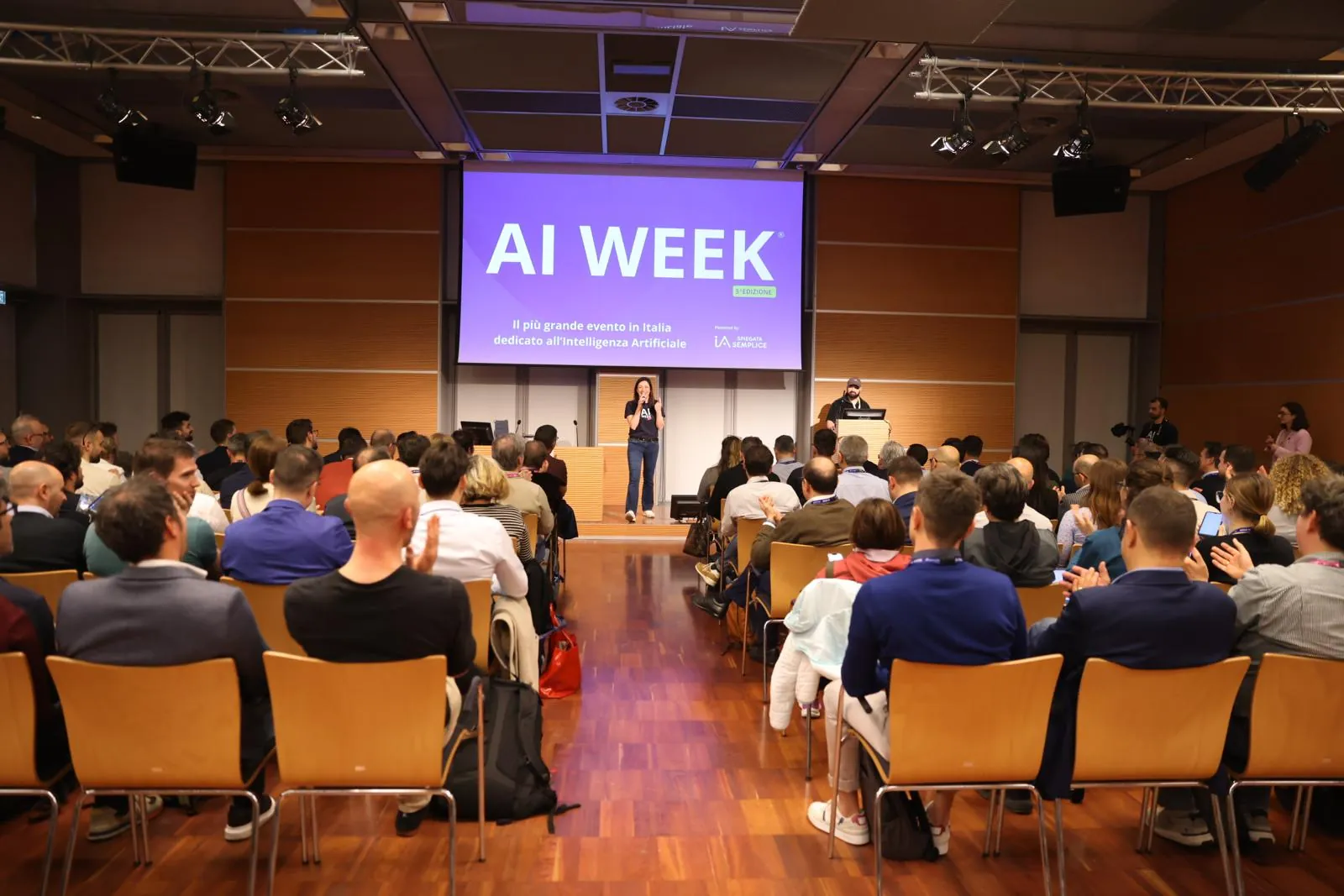 La sala di AI Week durante un intervento, con il pubblico seduto e lo schermo con il logo AI Week