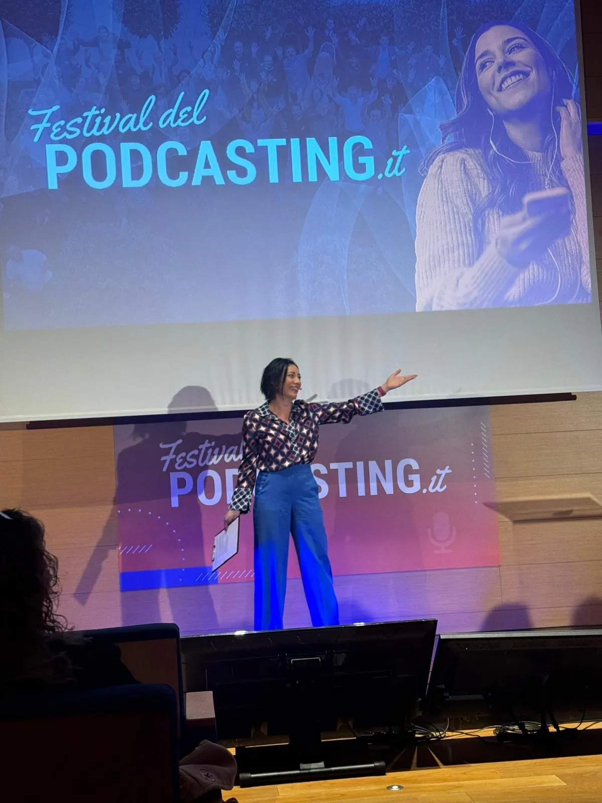 Alessia Preda sul palco principale del Festival del Podcasting con il braccio teso verso lo schermo