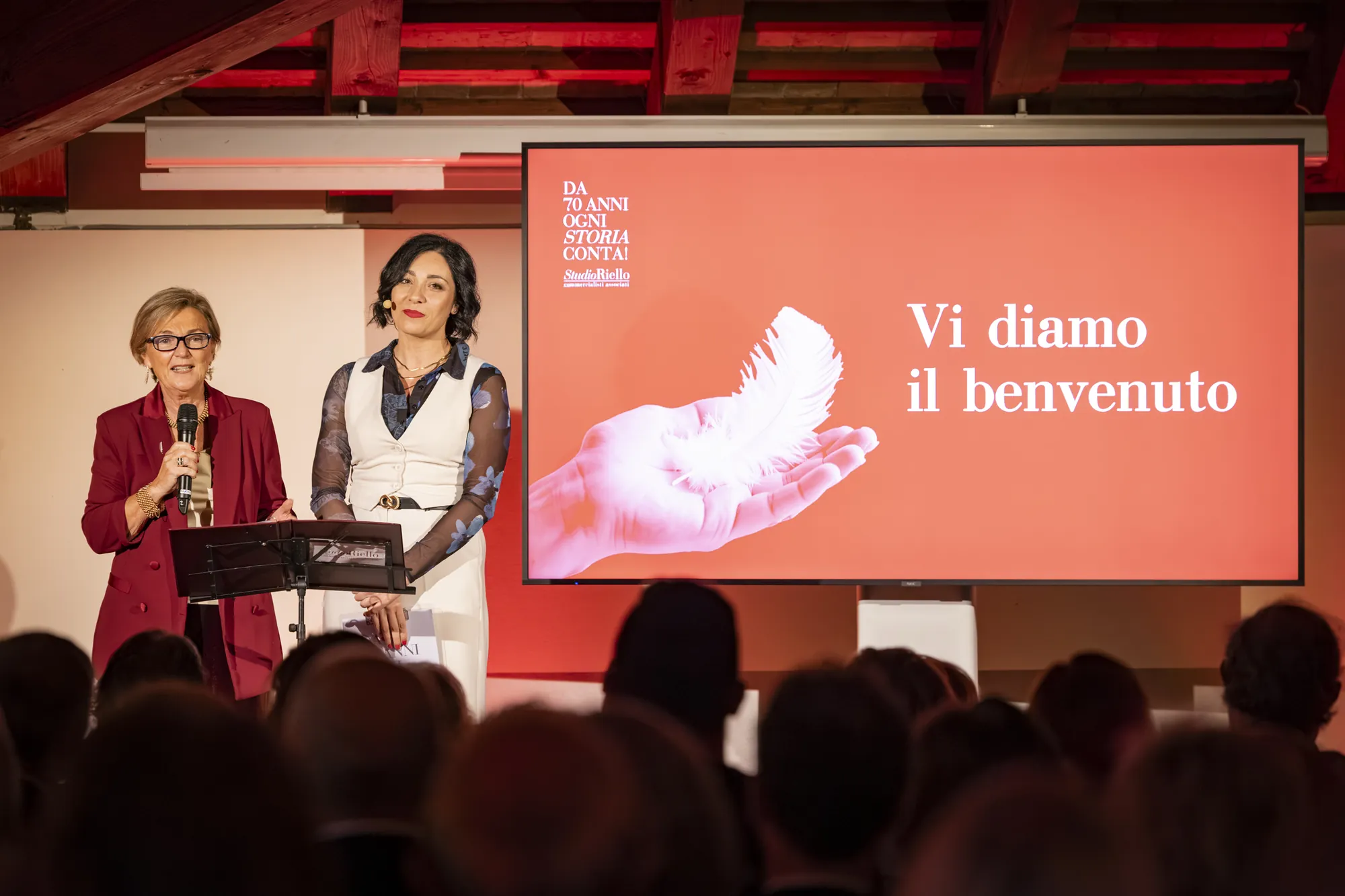 Alessia Preda sul palco con una persona dello Studio, davanti allo schermo «Vi diamo il benvenuto»