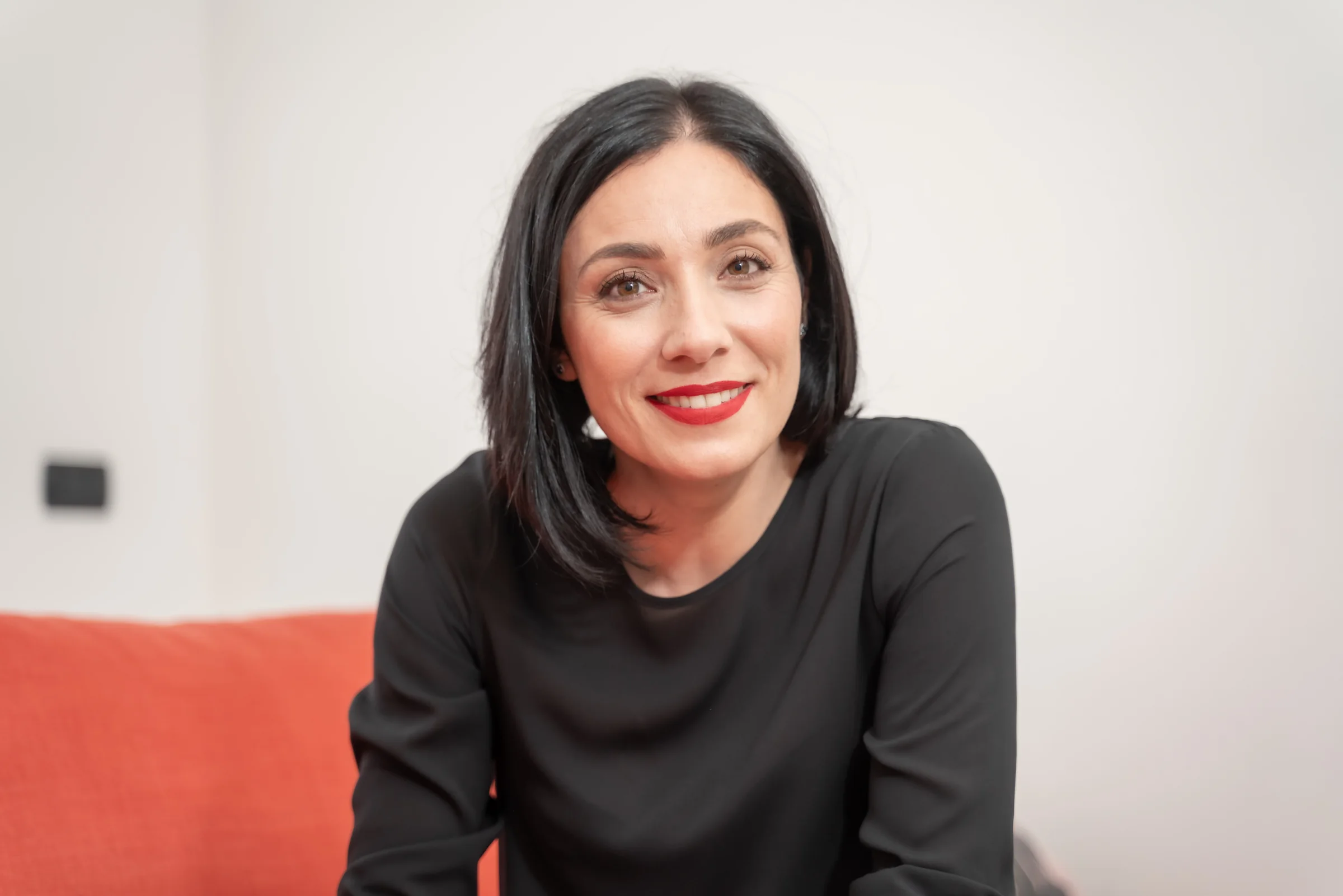 Alessia Preda sorridente, seduta su un divano corallo
